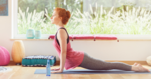 Лице прави йога поза върху постелка пред голям прозорец в слънчева стая