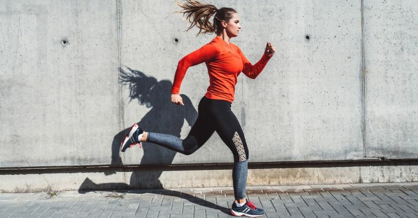 Жена тича по тротоара, облечена в спортно облекло