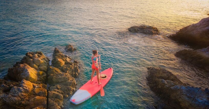 Човек гребе на сърф между скали в открито море