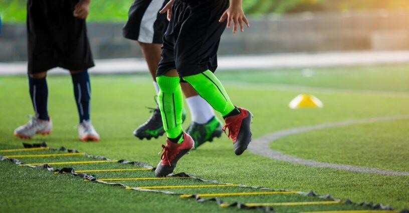 Футболист тренира бягане встрани с координационна стълба