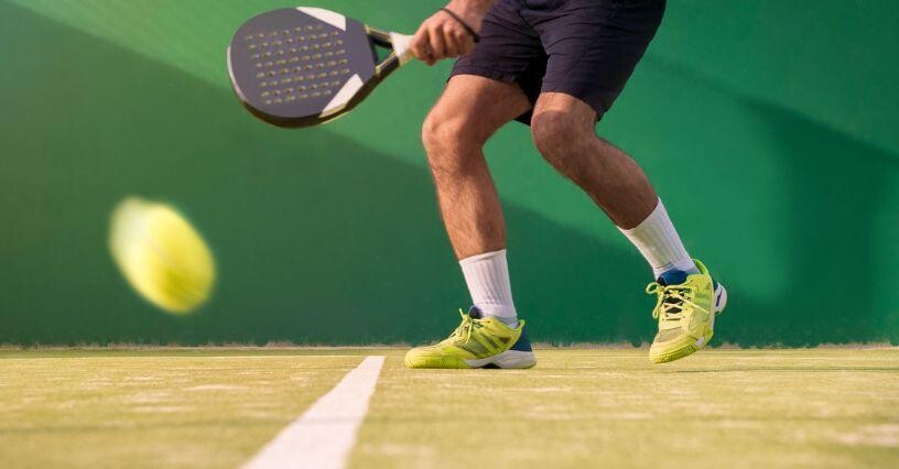 Човек играе падел, удряйки топка с ракета на корта