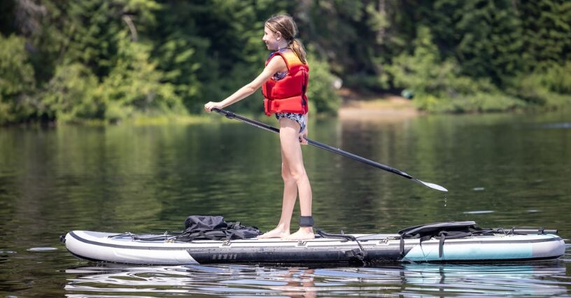 Дете на SUP дъска във вода, носещо спасителна жилетка